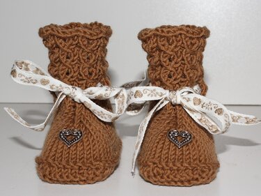 Braune gestrickte Babyschuhe mit gewelltem Schaft, weißen Schleifenbändern und kleinen Herzknöpfen