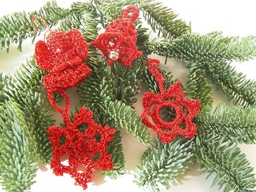 Rote gehäkelte Weihnachtsanhänger (Engel, Glocke, Stern, Schneeflocke) auf Tannenzweigen.