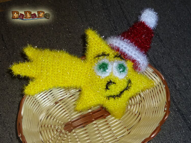 Gehäkelter gelber Stern mit grün-weißen Augen und roter Weihnachtsmütze auf geflochtenem Korb