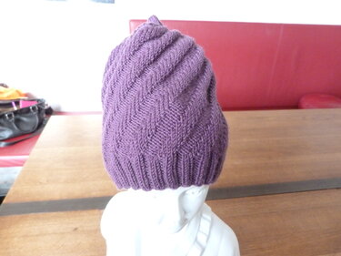 Lila gestrickte Mütze mit Fischgrätmuster auf weißem Mannequinkopf.