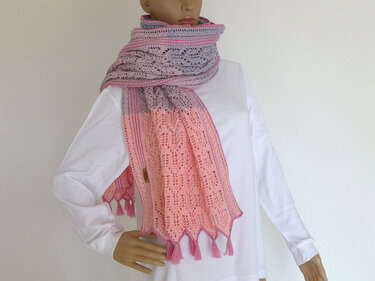 Gehäkelter Schal in Rosa- und Lilatönen mit Lochmuster und Quasten an einer Schaufensterpuppe