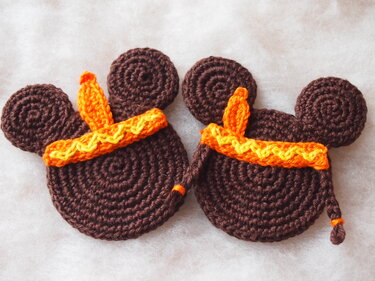 Two brown crocheted appliques with round ears and orange and yellow headbands; the right applique has a short braided tail.