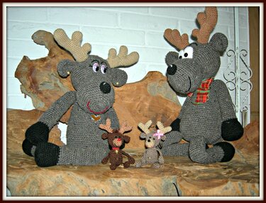 Zwei große graue gehäkelte Rentiere mit Geweihen und zwei kleine Amigurumi-Rentieranhänger auf Holzdeko