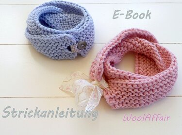 Zwei gestrickte Babyschals auf hellem Holz: hellblauer Loopschal mit Knopf und rosa Loopschal mit dekorativem Band.