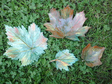 Vier handgeformte Blätter aus Modelliermasse in türkis-grün-braunen Tönen auf Gras