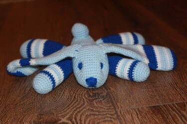 Handgearbeitet wirkender Amigurumi-Hase mit blauen Streifen und langen Ohren auf Holzboden