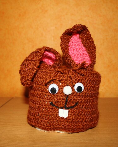 Braune gehäkelte Hülle mit Hasenohren, rosa Innenohren, Wackelaugen und weißen Vorderzähnen