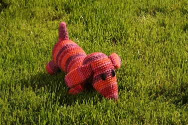 Gehäkelter gestreifter Amigurumi-Hund in Rosa und Orange auf Gras