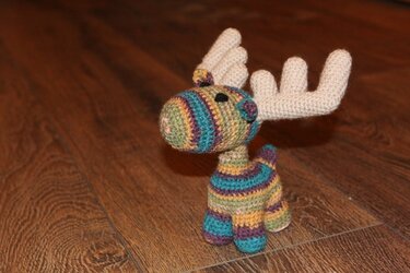 Gehäkelter gestreifter Amigurumi-Elch mit hellen Geweihen auf Holzfußboden