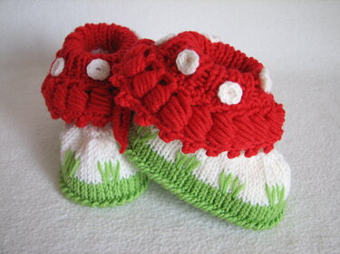 Nahaufnahme zweier gestrickter Babyschuhe in Fliegenpilz-Form auf hellem Untergrund