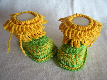Nahaufnahme von gestrickten Babyschuhen mit gelbem Rüschenrand und grün-gelben Fußteilen