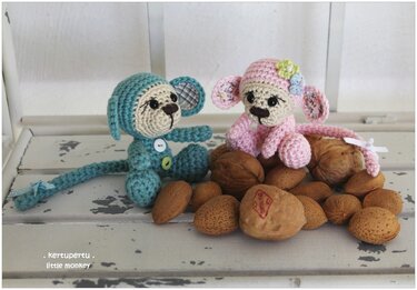 Gehäkelte Amigurumi-Affen in Rosa und Türkis mit Knopfdetails neben Nüssen