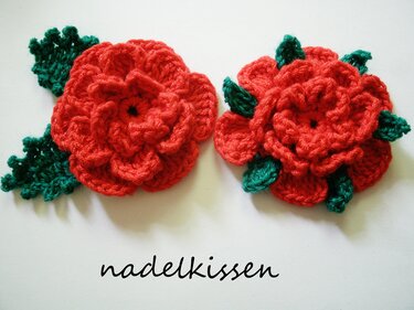 Zwei handgehäkelte rote Rosen mit grünen Blättern, Nahaufnahme