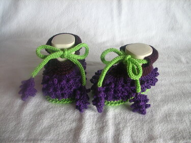 Detailaufnahme gestrickter lila Babyschuhe mit Rüschen und grüner Kordel
