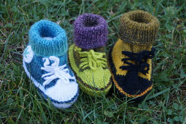 Drei gestrickte Babyschuhe im Sneaker-Stil in Blau-Weiß, Hellgrün und Gelb-Schwarz auf Gras
