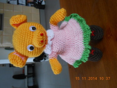 Gehäkeltes gelbes Schweinchen mit rosa Kleid und grünem Saum, zeigt Details von Proportionen und Nähten.