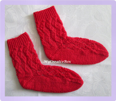 Paar rote handgestrickte Socken mit Zopfmuster auf hellem Untergrund