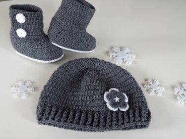 Gehäkelte graue Babymütze mit Blüten‑Applikation und passende Stiefel mit weißen Knöpfen, dekorative Häkelblüten daneben