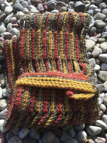 Folded striped crocheted cowl in mustard, rust and charcoal gray on pebbles