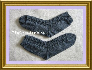 Paar grauer handgestrickter Socken mit Rippenbündchen und Zopfmuster auf hellem Untergrund