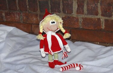 Gehäkelte Weihnachtswichtel-Puppe in roter Jacke und Zipfelmütze mit blonden Zöpfen und gehäkelter Zuckerstange