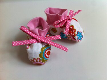 Genähte Babyschuhe aus gemustertem Stoff mit rosa Bündchen und gepunkteten Bindebändern