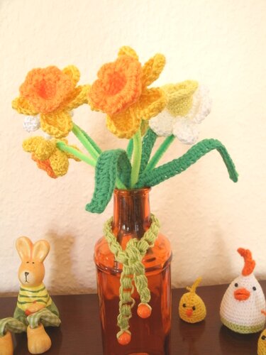 Gehäkelte Narzissen in bernsteinfarbener Vase mit gehäkelten Osterfiguren (Hase, Küken, Huhn)