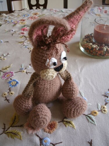 Handgehäkelter brauner Amigurumi-Hase mit langen Ohren und runden Augen auf bestickter Tischdecke