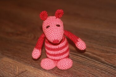 Gehäkelte Amigurumi-Maus rot-rosa gestreift auf Holzboden