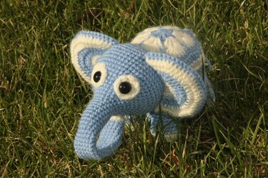 Handgehäkelter Elefant in Hellblau und Creme auf grünem Gras.