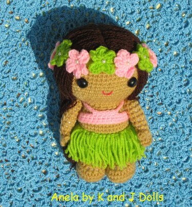 Crocheted amigurumi hula doll wearing green fringe skirt, pink top and a flower crown