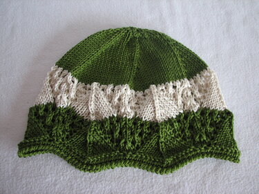Grün-weiße gestrickte Babymütze mit Struktur- und Lochmuster und gewelltem Rand auf hellem Untergrund