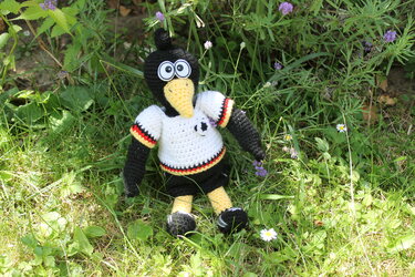 Gehäkelter Amigurumi-Vogel in Deutschland-Trikot mit Fußballmotiv sitzt im grünen Gras