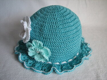 Gehäkelte türkise Babymütze mit weißen und hellblauen Blumen und gewelltem Rand