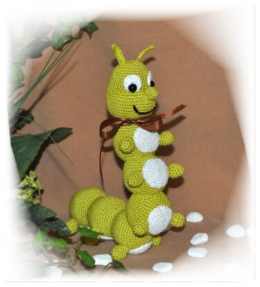 Grüne gehäkelte Amigurumi-Raupe mit weißen Bauchflecken und brauner Schleife