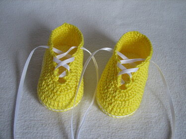 Gehäkelte gelbe Babyschuhe mit weißen Schnürbändern auf hellem Stoff