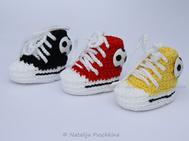 Drei gehäkelte Baby-Sneaker in Schwarz, Rot und Gelb mit weißen Schnürsenkeln und Fußball-Knöpfen