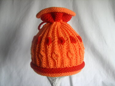 orange-rote gestrickte Babymütze mit Zopfmuster, roten Herzmotiven und Kordelzug