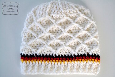 Cremeweiße gehäkelte Mütze mit erhabenem Rautenmuster und schwarzen, roten und gelben Streifen am Saum