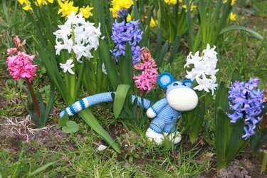 Blau-weißes Amigurumi mit gestreiftem Schwanz zwischen Hyazinthen und Narzissen