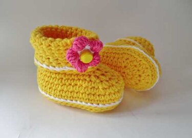 Gehäkelte gelbe Babyschuhe mit weißer Kante und rosa Blüte, Nahansicht