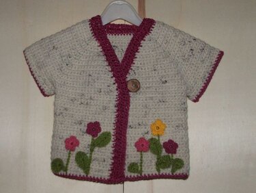 Cremefarbene gehäkelte Babyjacke mit pinker Einfassung, Blumenapplikationen und Holzknopf