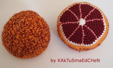 Zwei handgehäkelte Orangen, eine ganze und eine geschnittene Scheibe mit dunklem Innenleben.
