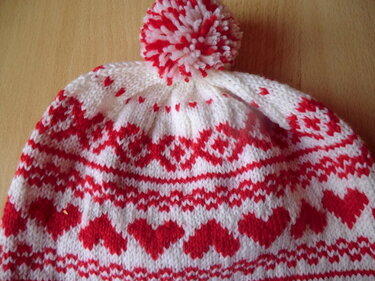 Weiß-rote gestrickte Kindermütze mit Herz- und Norwegermuster und Bommel