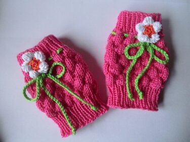Rosa gestrickte Baby-Stulpen mit weiß-orangener Blüte und grüner Kordelschleife