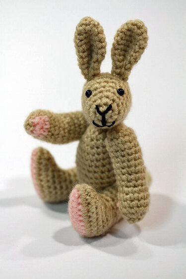 Kleiner sitzender gehäkelter Hase in Beige mit rosa Pfoten und Ohren.