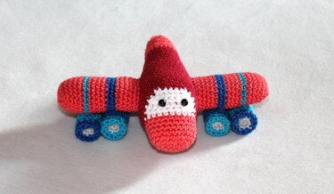 Gehäkeltes Amigurumi-Flugzeug in Rot und Blau mit schwarzen Augen und vier Rädern