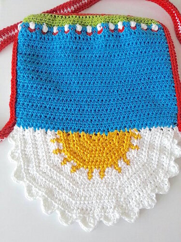 Farbenfrohe gehäkelte Umhängetasche in Blau, Weiß, Gelb und Rot mit Sonnenmotiv und gestreiftem Riemen.
