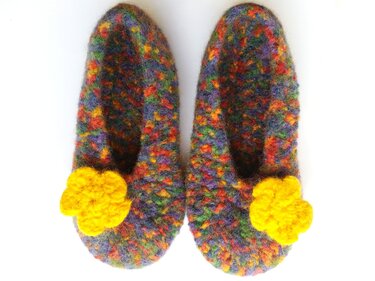 Bunte gefilzte Hausschuhe mit gelber Häkelblüte auf weißem Hintergrund.