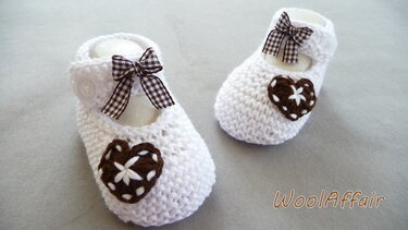 Weiße gestrickte Babyschuhe mit braunem Herz und kariertem Schleifchen